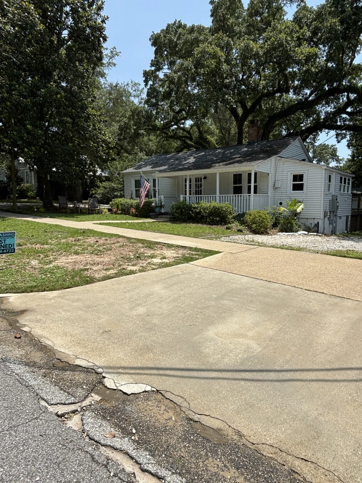 After: soft-washed white Fairhope cottage under oaks with JUST CLEANED sign
